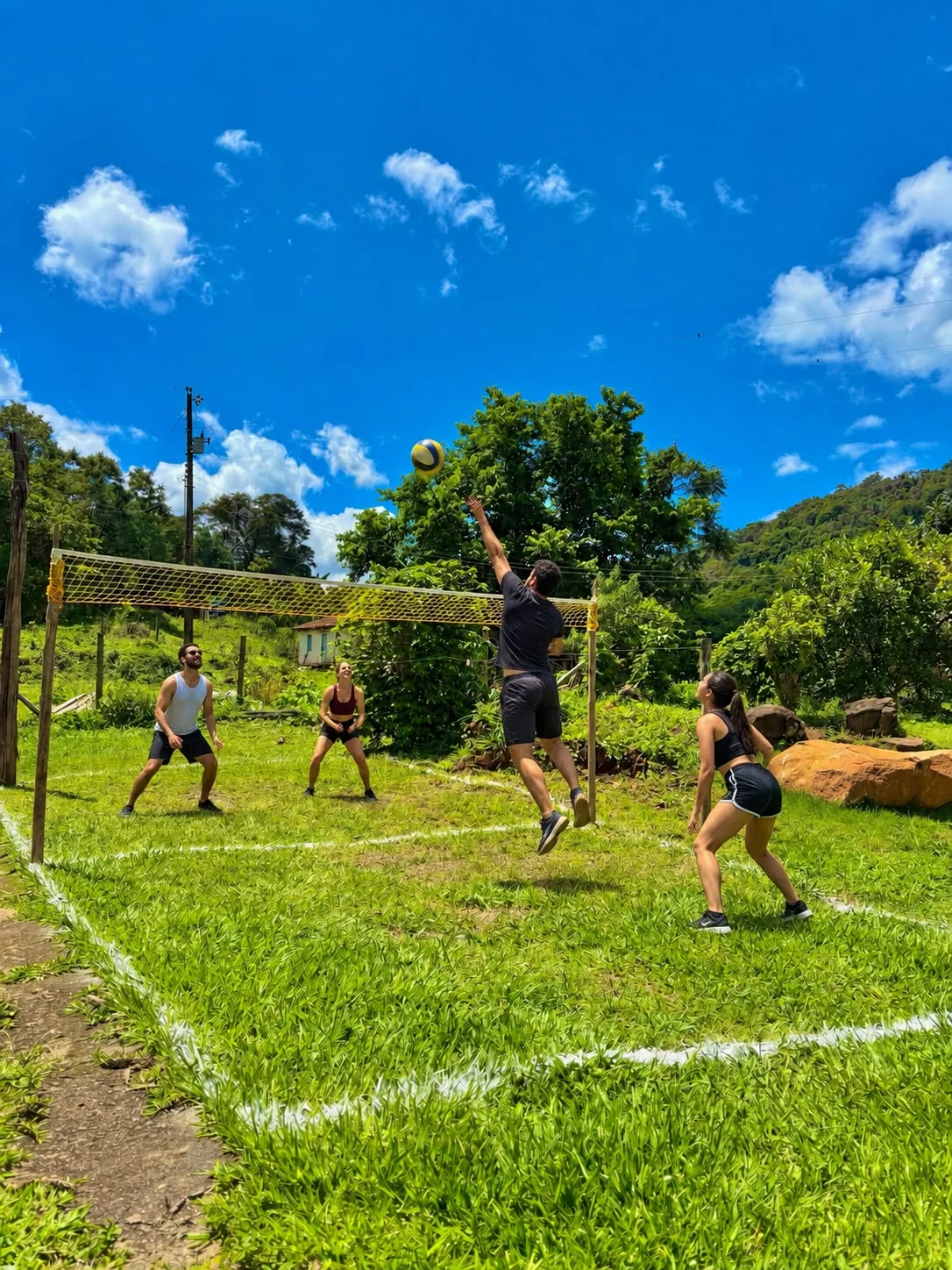 Hóspedes jogando vôlei na área gramada com rede do Sítio da Barra